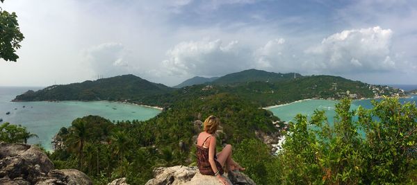 High angle view of woman sitting on cliff against sky