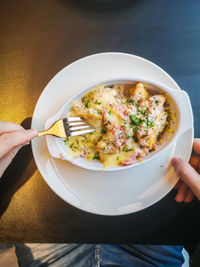 A man eats baked dumplings with a sauce of bacon, ham, herbs and cheese.