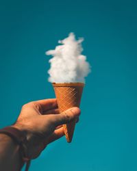 Midsection of person holding ice cream against blue sky