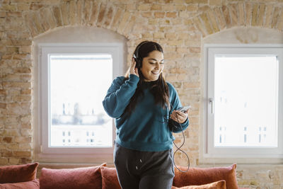 Smiling woman enjoying listening to music through headphones at home