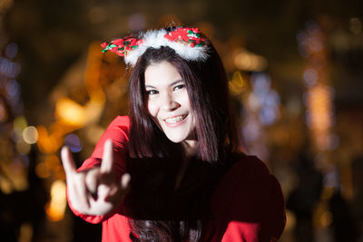 Portrait of smiling young woman gesturing while wearing headwear at night