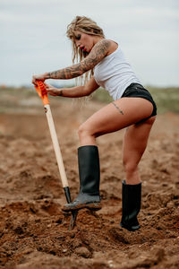 Young woman standing on the sand and digging with a shovel