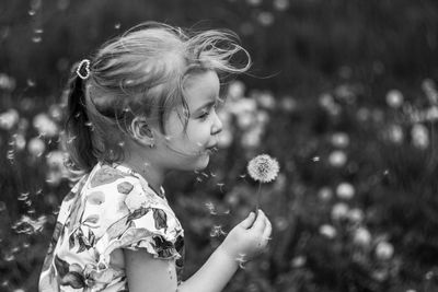 Side view of girl standing holding dandelion against blurred background