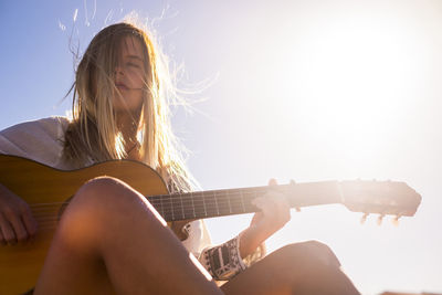 Close-up of woman playing guitar against sky on sunny day