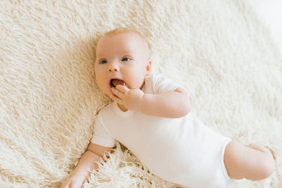 Baby boy lies on a light blanket and holds his hand in his mouth, teeth are teething
