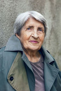 Portrait of an old siniors grandmother of 90 with gray hair stands against a gray wall on the street