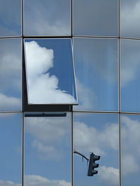 Low angle view of modern building with only one open window and reflection of traffic lights and sky