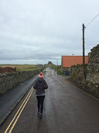 Full length rear view of woman jogging on road against sky during winter