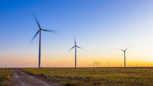 Wind turbines in field against blue sky and sunset