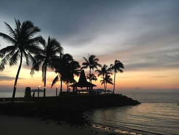 Silhouette palm trees by swimming pool against sky during sunset