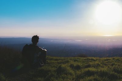 Rear view of man sitting on grassy field against sky