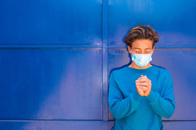 Portrait of young man standing against blue wall