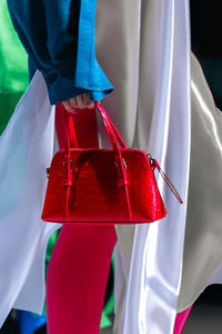 White silk long dress and small red handbag in a woman's hand. elegant clothing and accessories.