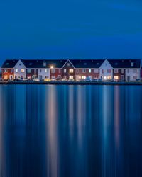 Illuminated buildings by sea against sky at night