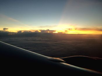 Cropped image of airplane flying over landscape against sky during sunset