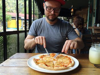 Young man eating pizza while sitting at table in restaurant