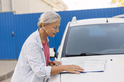 Senior woman looking at road map on her car bonnet