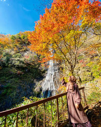 Woman standing by railing against trees during autumn