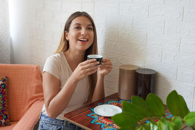 Beautiful young woman drinking coffee sitting on table at home