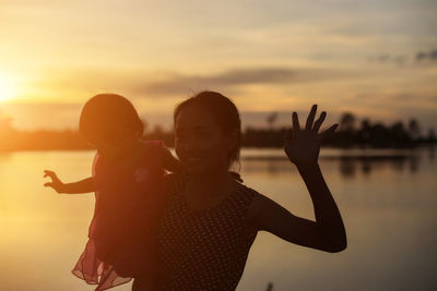 Friends with arms raised against sky during sunset