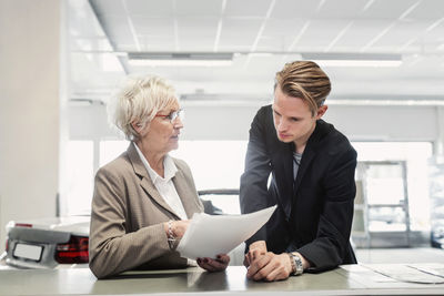 Two sales colleagues discussing documents at car dealership