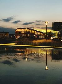 Illuminated street light by river against sky at sunset