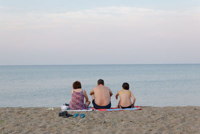 Rear view of men sitting on beach against sky