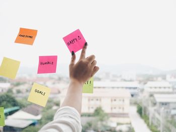 Cropped hand of businesswoman sticking colorful adhesive notes on window in office