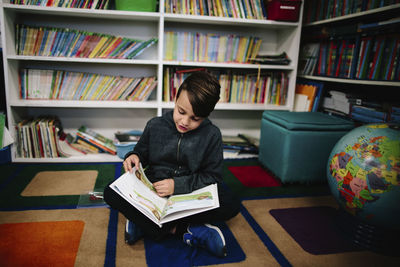 Boy studying while sitting against bookshelves in library