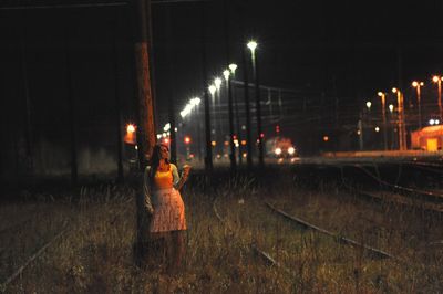 Woman standing on grassy land by pole at night