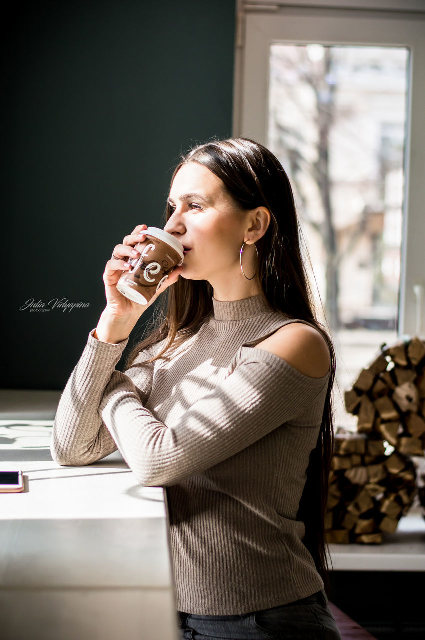 one person, holding, young women, indoors, young adult, waist up, women, hairstyle, adult, hair, standing, casual clothing, long hair, food and drink, front view, real people, lifestyles, leisure activity, beautiful woman, drinking, mouth open