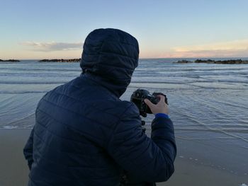 Rear view of man photographing at beach during sunset