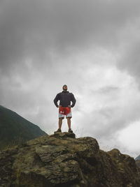 Rear view of man standing on mountain against cloudy sky