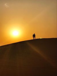Silhouette people riding on desert against sky during sunset