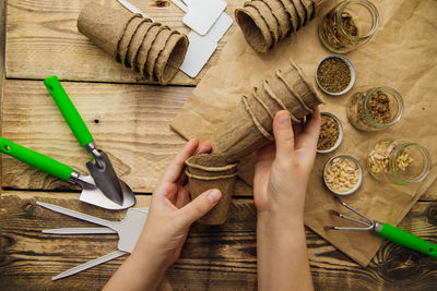 Women's hands hold peat pots. top view of seeds and garden tools on a wooden background.