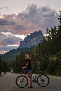 Woman with bicycle on road against mountains at dusk