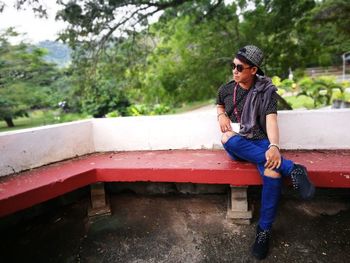 Young man wearing sunglasses while sitting on bench against trees