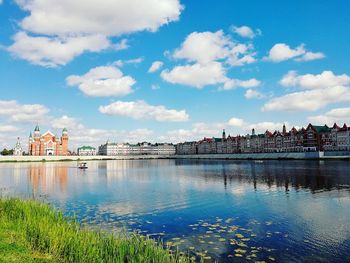 View of buildings by river against cloudy sky