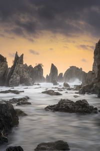 Rocks in sea against sky during sunset