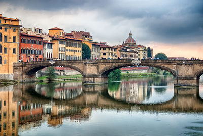 Arch bridge over river against cloudy sky