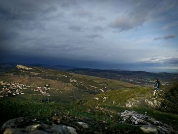 Mountain biker on peak over landscape against sky