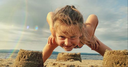 Portrait of girl over sandcastle at beach against sky