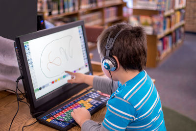A child with head phones works an interactive game on a laptop at the library