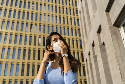 Young businesswoman wearing face mask against office building during covid-19 outbreak