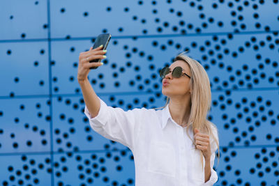 Portrait of a young attractive woman taking a selfie with a smartphone on a blue background person