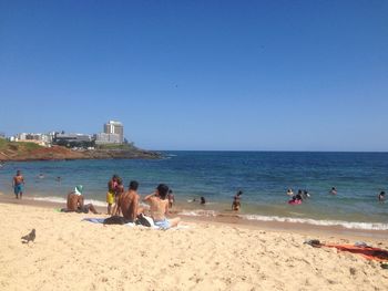 People on beach against clear blue sky