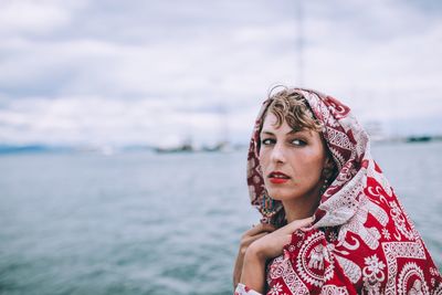 Portrait of young woman wearing headscarf while standing against sea