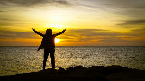 Silhouette woman standing on rock against sea during sunset