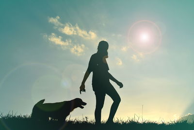 Silhouette woman and dog walking on grassy field against sky during sunset