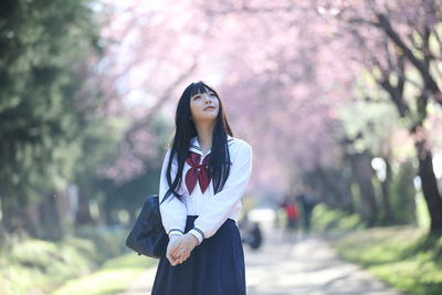 Young woman standing by tree against plants